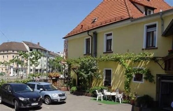 A yellow building with a red roof, parked cars, and outdoor seating. - Hotel Rose Heidelberg (Heidelberg)