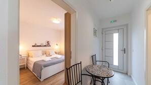 Une chambre à coucher comprenant un lit, des tables de chevet, une commode, une étagère murale décorative, une fenêtre et une porte.