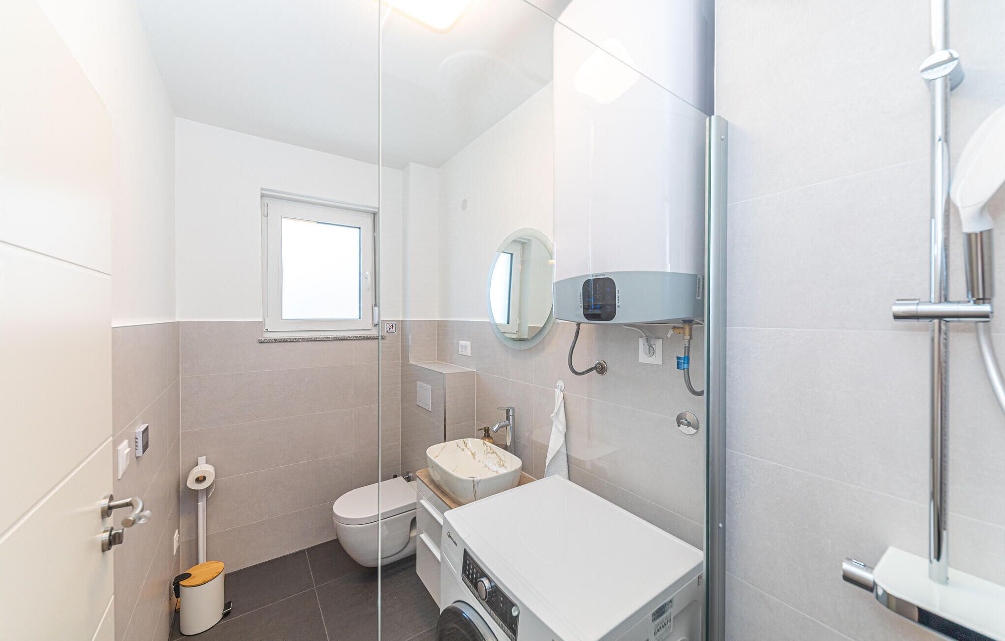A modern bathroom with a glass shower enclosure, a toilet, a sink, and a washing machine.