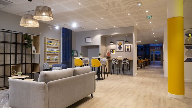 A modern hotel lobby with a sofa, yellow chairs, a bar area, and a wooden floor. - Appart Hotel Odalys City Le Havre Les Docks (Le Havre)