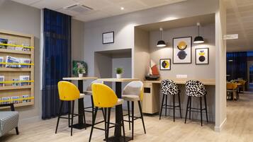 A modern bar area with yellow and black patterned stools, a wooden bookshelf, and framed artwork on the wall.