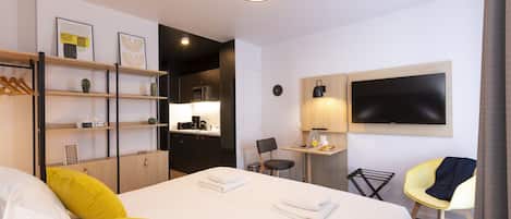A hotel room with a bed, a desk, a chair, a TV, and a shelf with decorative items.