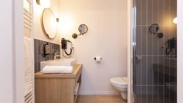 A modern bathroom with a wooden vanity, a large mirror, a handheld hair dryer, and a toilet.