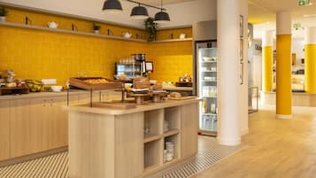 A modern kitchen area with a yellow-tiled backsplash, wooden cabinets, and a central island with food items and a coffee machine.