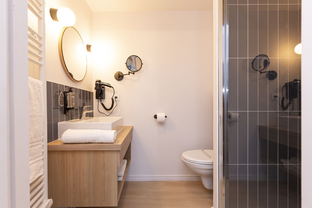 Un baño moderno con tocador de madera, un espejo grande y cabina de ducha de vidrio.