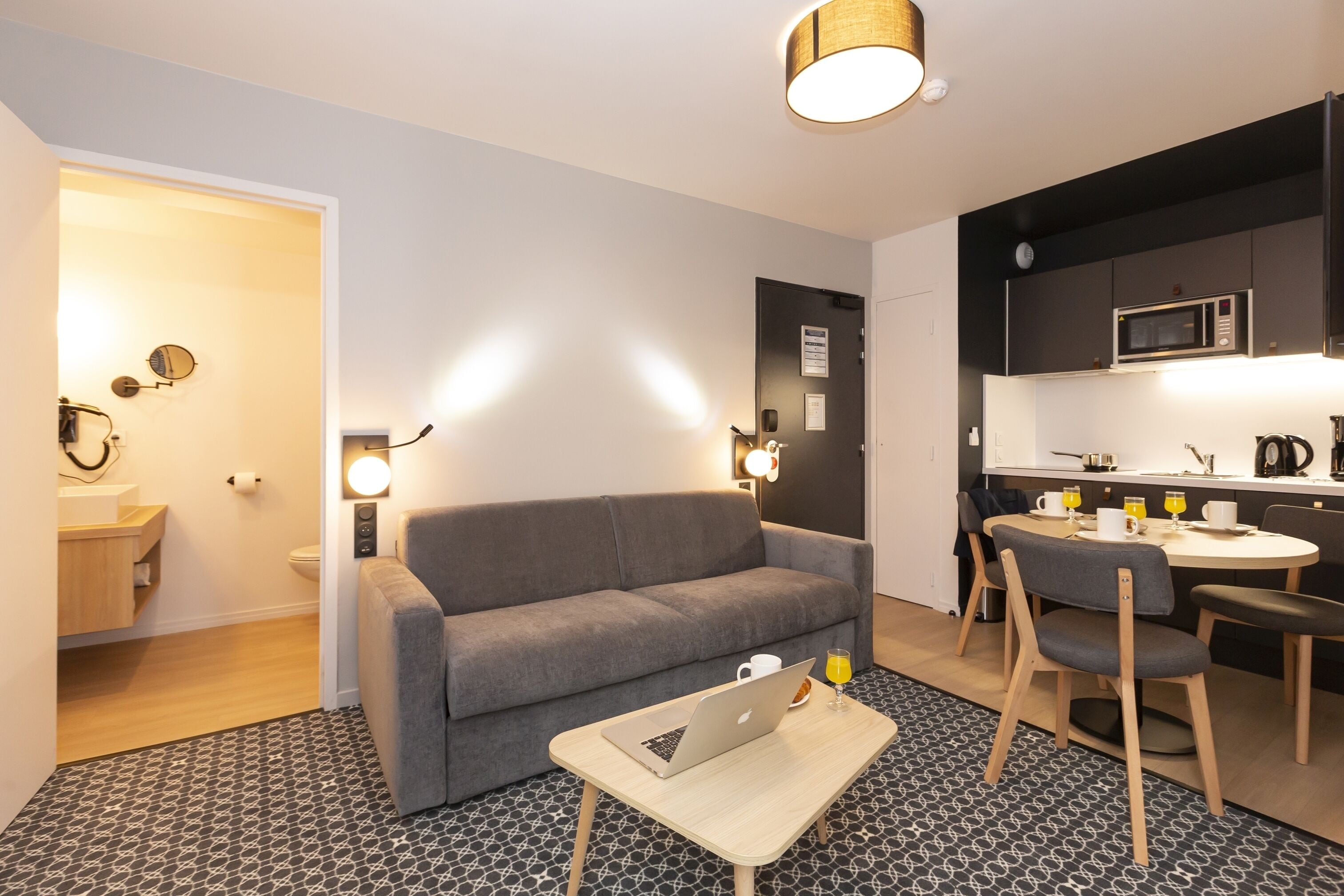 A modern living room with a grey sofa, a small table with a laptop, and a patterned floor.