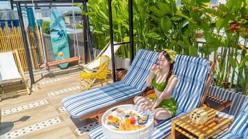 A person relaxing on a striped lounge chair with a tray of food and drinks.