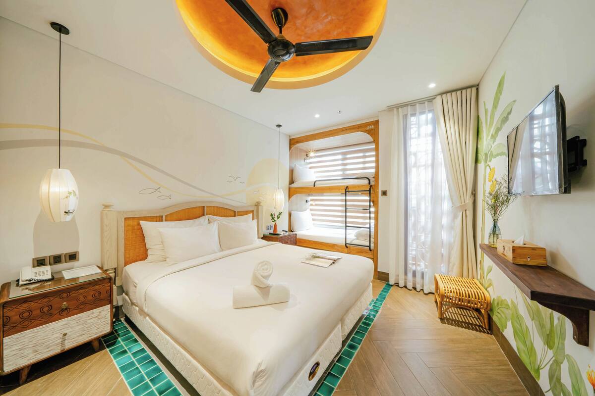Una habitación de hotel con una cama grande, un ventilador de techo, un televisor y una ventana con cortinas.