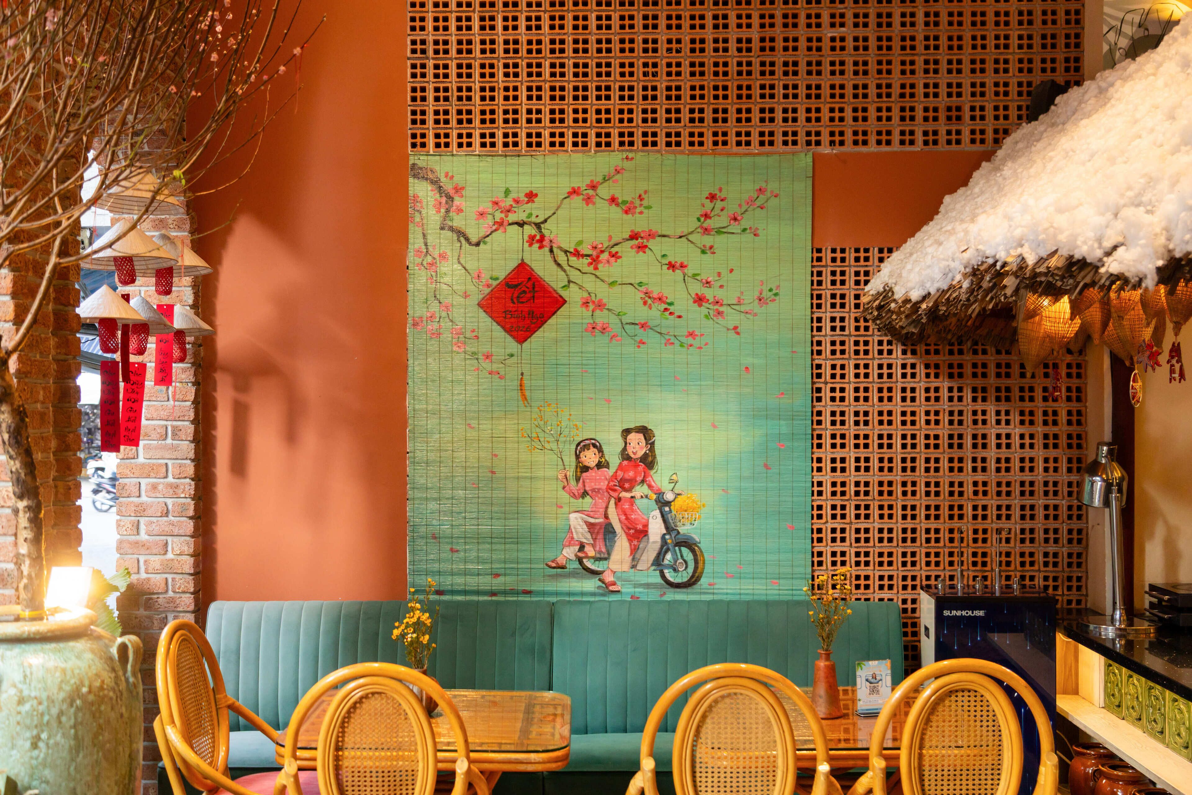 Une pièce au décor traditionnel, avec un canapé vert, des fauteuils en osier, un mur décoratif orné d’un tableau, et un mur en briques agrémenté de décorations suspendues.
