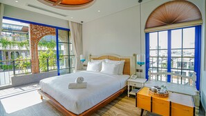 Une chambre d’hôtel avec un grand lit, une table de chevet en bois, une petite table et une vue sur la ville grâce à de grandes fenêtres.