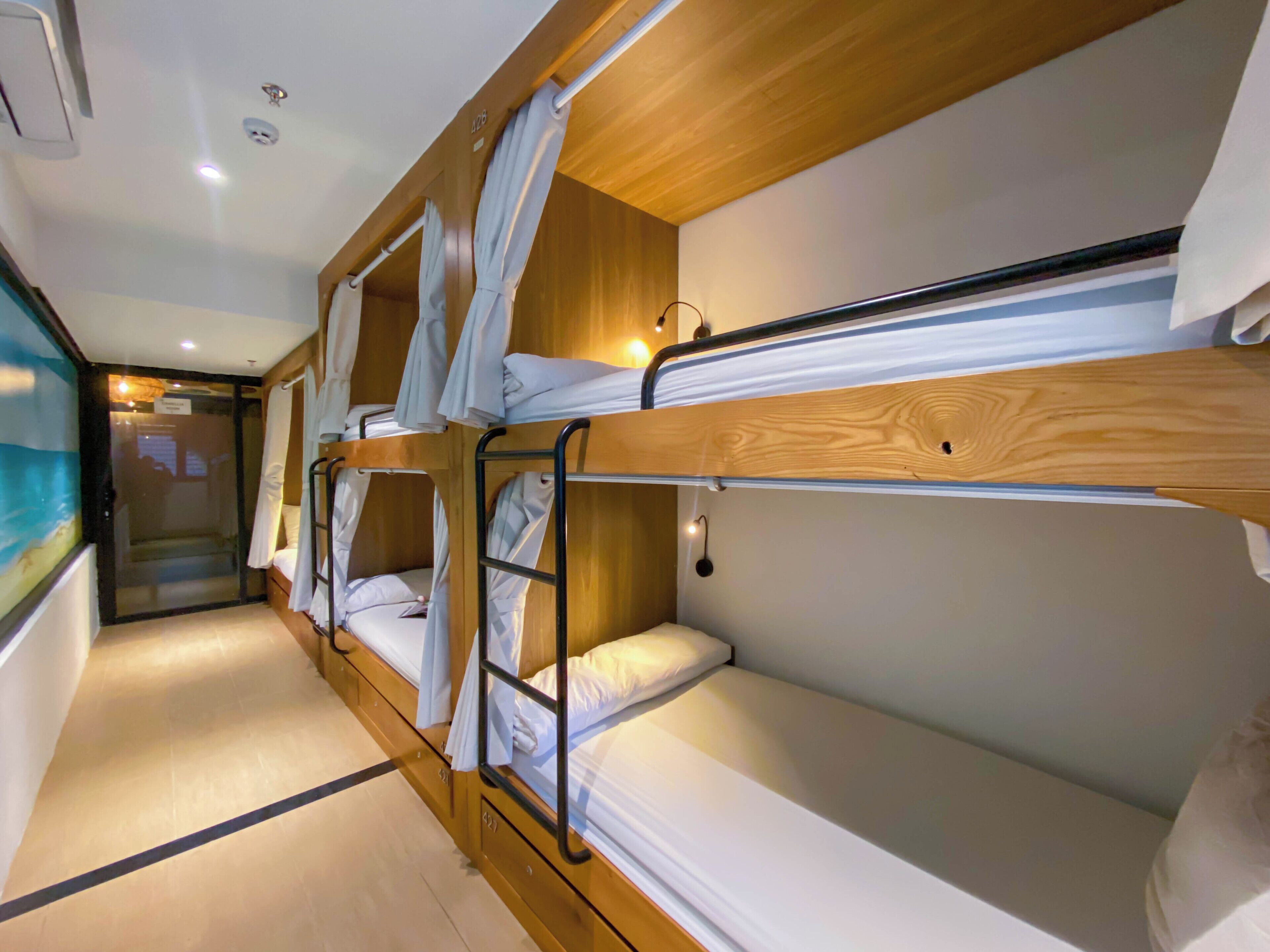 Une chambre avec des lits superposés, des têtes de lit en bois, une literie blanche et une petite lampe fixée au mur.