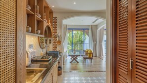 Une cuisine moderne avec des étagères en bois, un coin repas avec une table et des chaises, et une vue sur la verdure à l’extérieur.