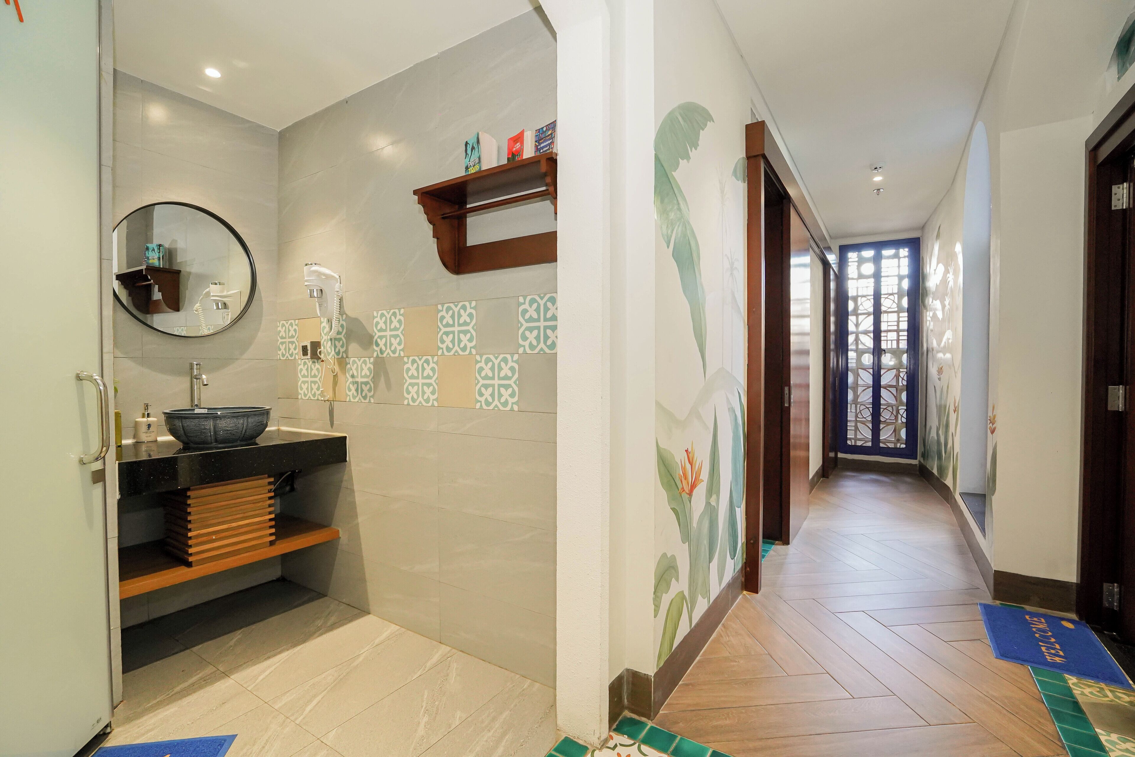 Un pasillo con un baño a la izquierda, que incluye un lavamanos, espejo y perchero. El pasillo tiene baldosas estampadas y suelo de madera.