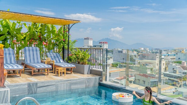 Une piscine à débordement située sur le toit, avec des chaises longues et une vue sur le paysage urbain.