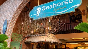 Une enseigne pour « Seahorse Signature », avec le logo d’un hippocampe, un mur en briques et une structure surmontée d’un toit de chaume.