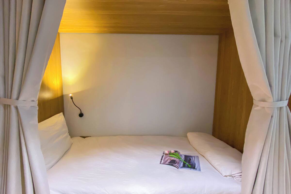 Una cama individual con sábanas blancas, una lámpara de noche y una revista sobre la cama.