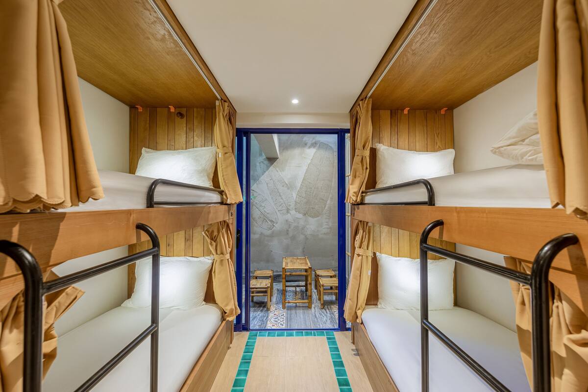 Habitación con literas, una pequeña mesa y sillas en el centro, paredes de madera y vistas a través de un ventanal.