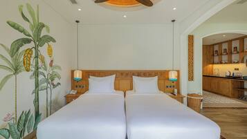 A hotel room with two beds, a ceiling fan, a kitchen area, and a mural of tropical plants.
