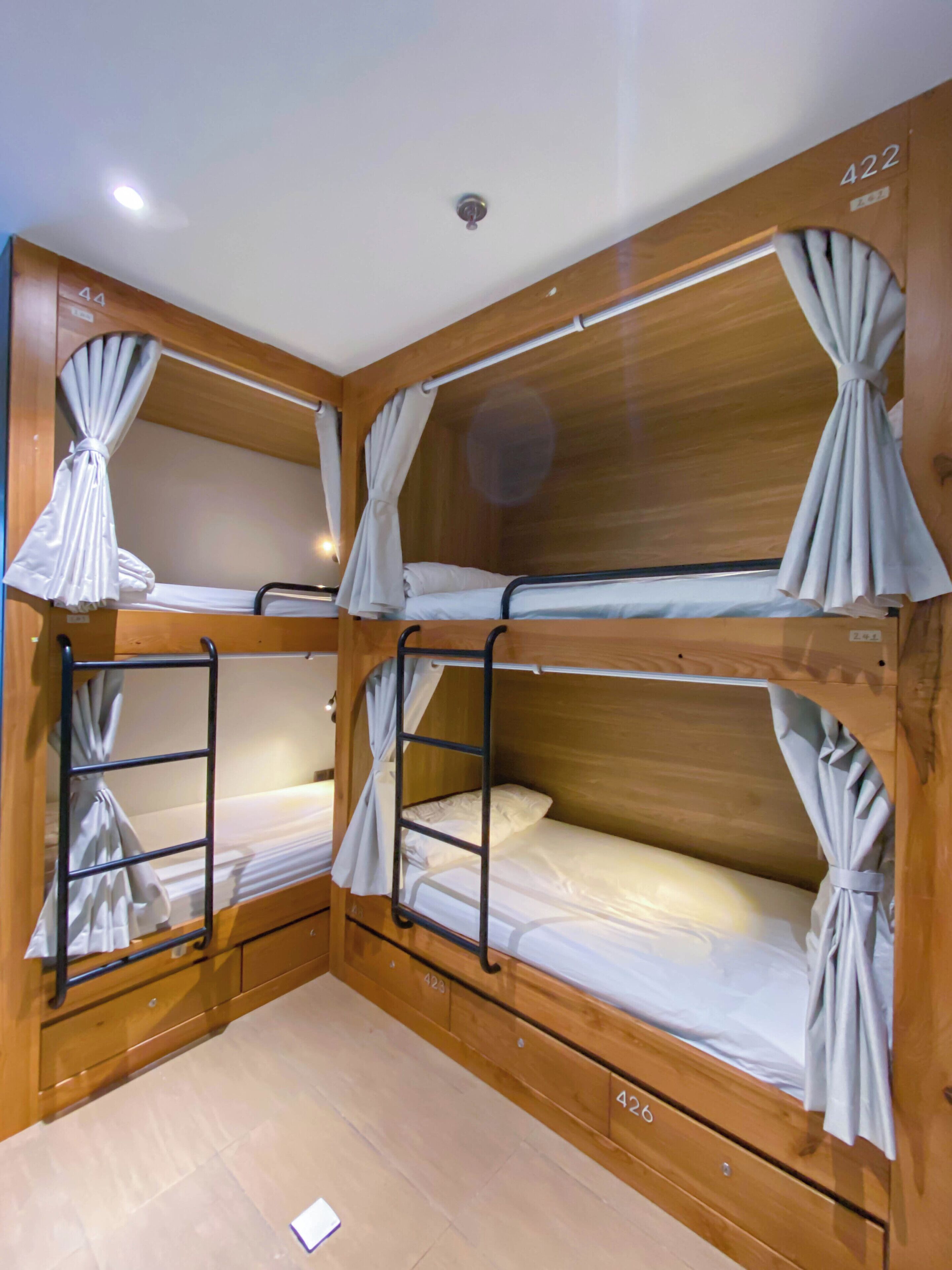 A corner room with three bunk beds, each with a curtain, and wooden walls with room numbers 422 and 426.