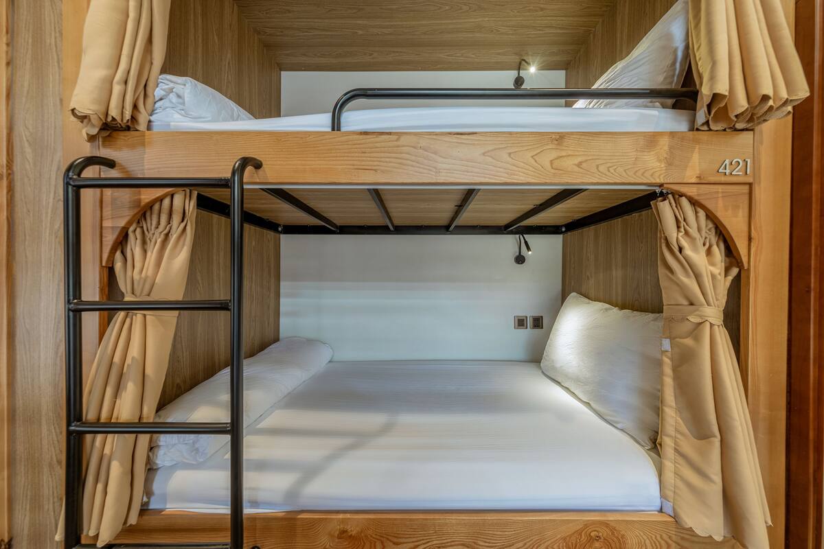 Una cama individual con estructura de madera, número 421, y cortinas color beige.