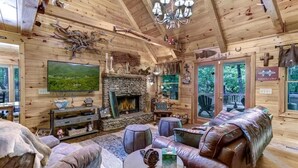 A cozy log cabin interior with a stone fireplace, leather furniture, and a large TV.
