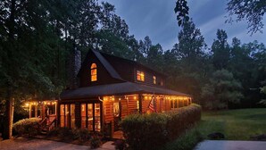 A log cabin with a porch, a stone chimney, and an American flag.