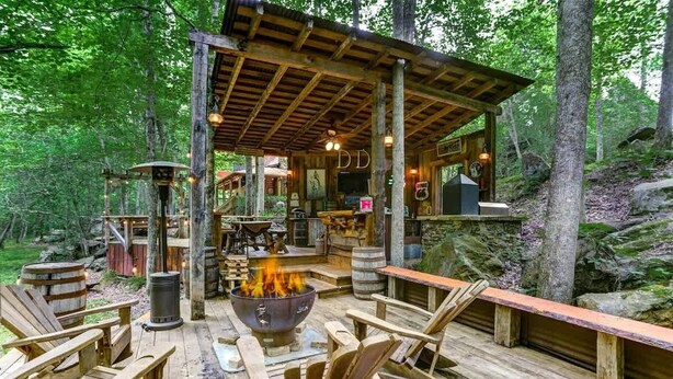 A rustic wooden deck with a fire pit, seating, and a covered area with a bar.