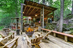 A rustic wooden deck with a fire pit, seating, and a covered area with a bar.
