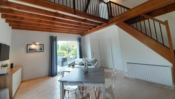 Amplia habitación con techo alto, vigas de madera, una mesa de comedor, sillas, un sofá y una escalera.