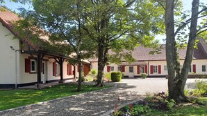 Un patio con un sendero de grava, rodeado de árboles y un edificio con contraventanas rojas.