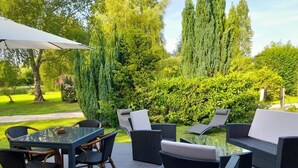 Un patio al aire libre con una mesa de vidrio y sillas de mimbre, rodeado de follaje y árboles.