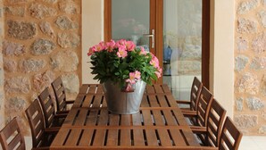 A stone wall with a wooden table and chairs, a metal bucket with flowers, and a wooden door. - Private villa with breathtaking views and private pool. (Port de Sóller)