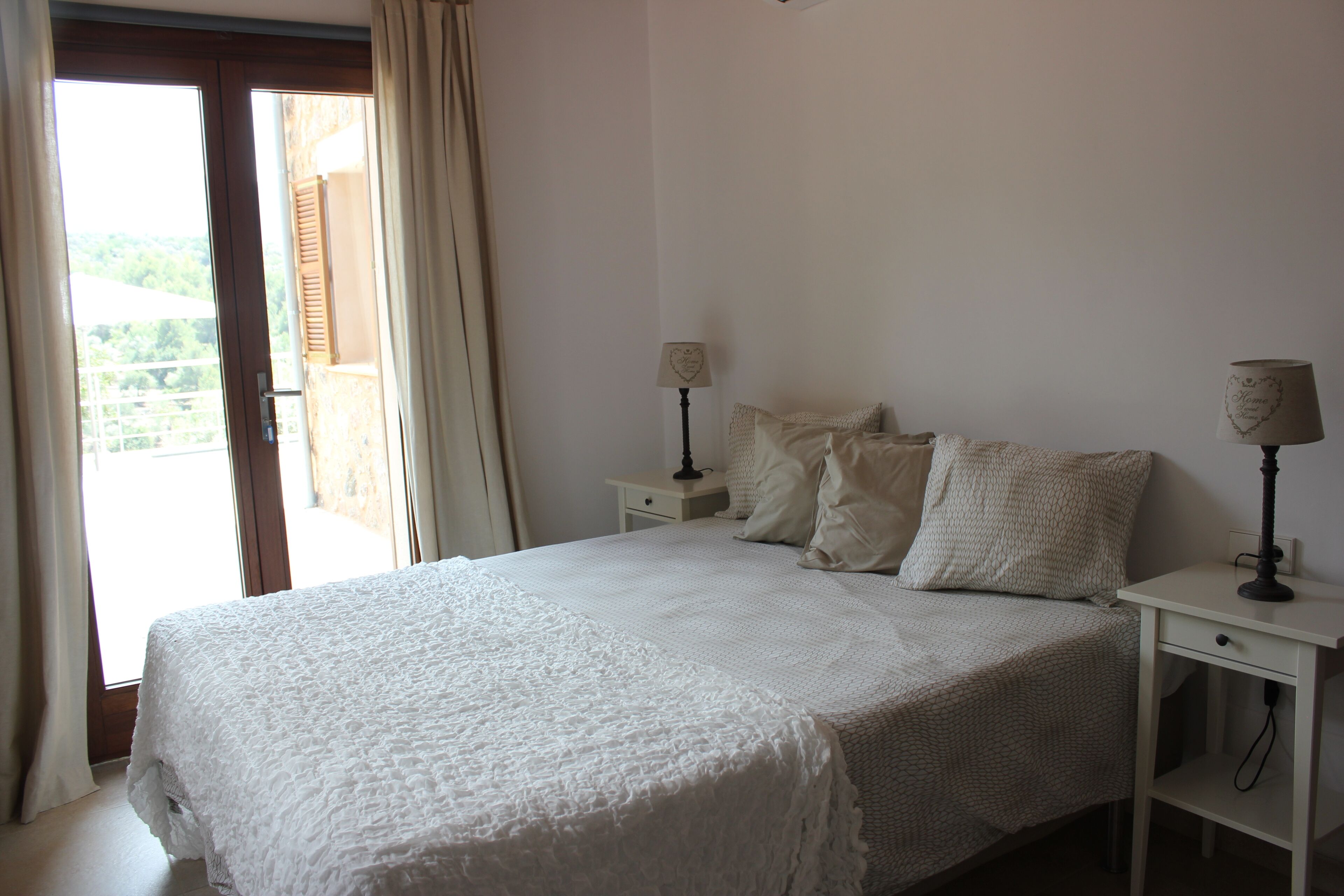 A bedroom with a large bed, two bedside tables, and a view through a window with curtains.
