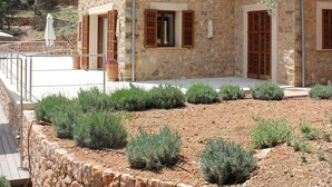 A stone house with wooden shutters, a stone retaining wall, and a small garden with shrubs. - Private villa with breathtaking views and private pool. (Port de Sóller)