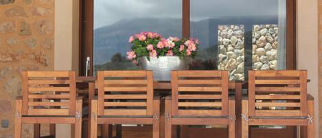 A wooden table with four chairs, a metal bucket with flowers, and a stone wall.