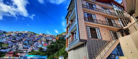 A multi-story building with a staircase and a view of a densely packed hillside with colorful houses.