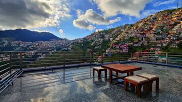 A terrace with a table and benches, overlooking a densely packed hillside with colorful buildings.