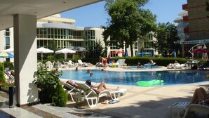 A pool area with lounge chairs, umbrellas, and a building with large windows in the background. - Hotel Klisura (Sunny Beach)