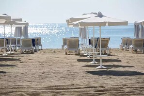 Une plage bordée de rangées de transats blancs et de parasols, disposés sur le sable.