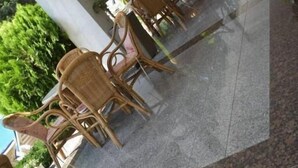 An outdoor seating area with wicker chairs and tables, surrounded by greenery and a tiled floor. - Hotel Klisura (Sunny Beach)