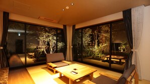 Una sala de estar moderna con una mesa de centro de madera, sofá y sillones, ventanas amplias con cortinas y vistas a un jardín.