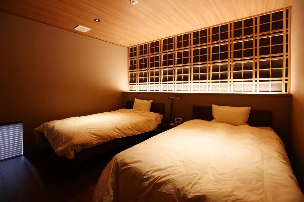 A room with two beds, a wooden ceiling, and a wall with a grid pattern.