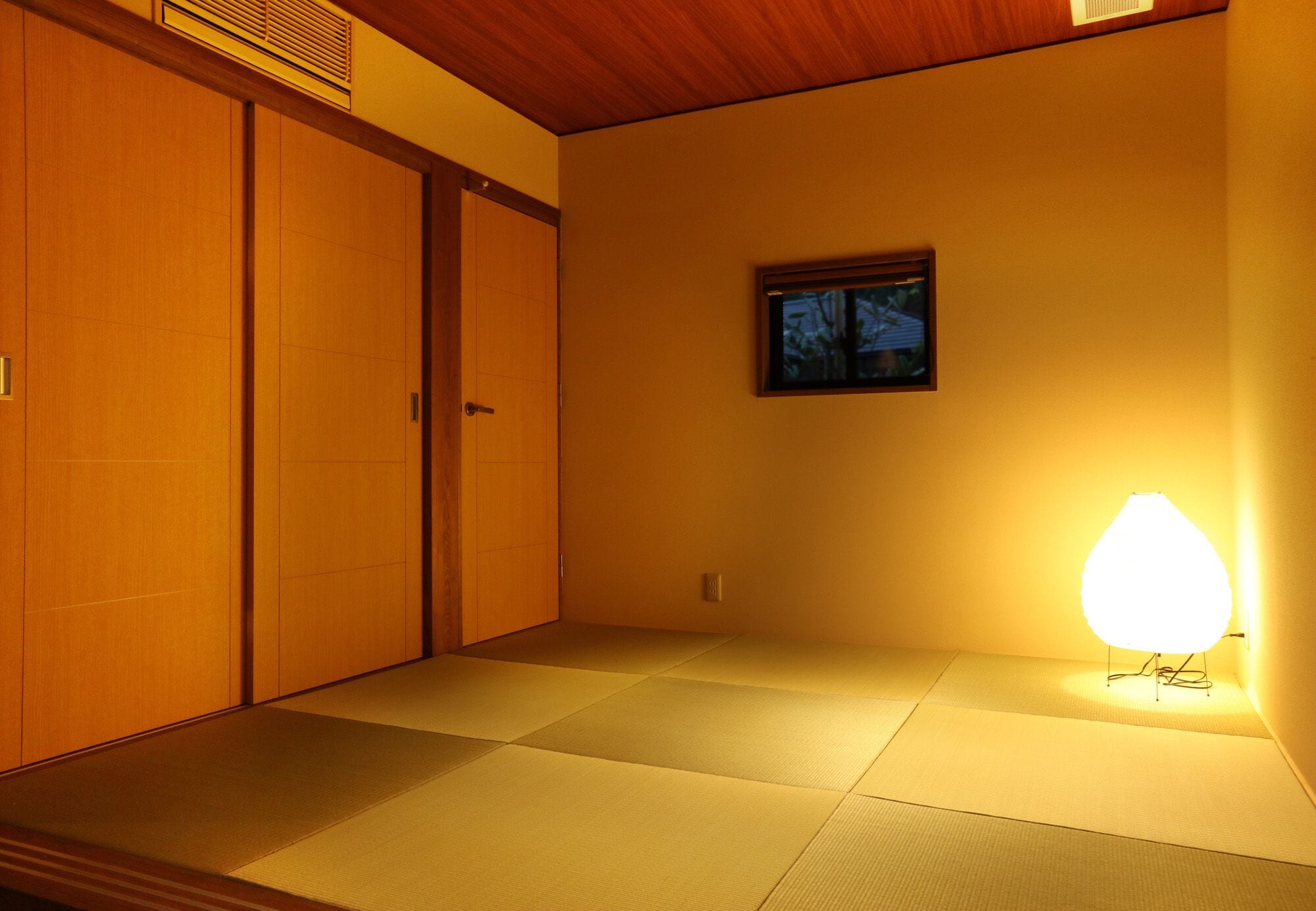 Une pièce avec un sol recouvert de tatamis, des portes coulissantes, un tableau accroché au mur et un lampadaire.