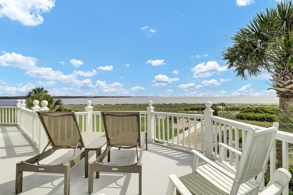 A deck with two chairs and a table overlooking a beach with a clear view of the ocean and distant shoreline.