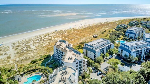 An aerial view of a coastal hotel with multiple buildings, a beach, and a swimming pool.