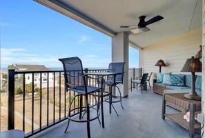 A balcony with two chairs, a table, a sofa, and a ceiling fan. - Fully Renovated 2025 | Oceanfront 2BR in Wild Dunes (Isle of Palms)