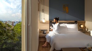 A hotel room with a bed, bedside table, and a view of the cityscape. - O by Tamara Coimbatore (Coimbatore)