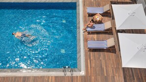 A swimming pool with a wooden deck, lounge chairs, and umbrellas. - O by Tamara Coimbatore (Coimbatore)
