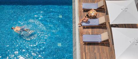 A swimming pool with a wooden deck, lounge chairs, and umbrellas.