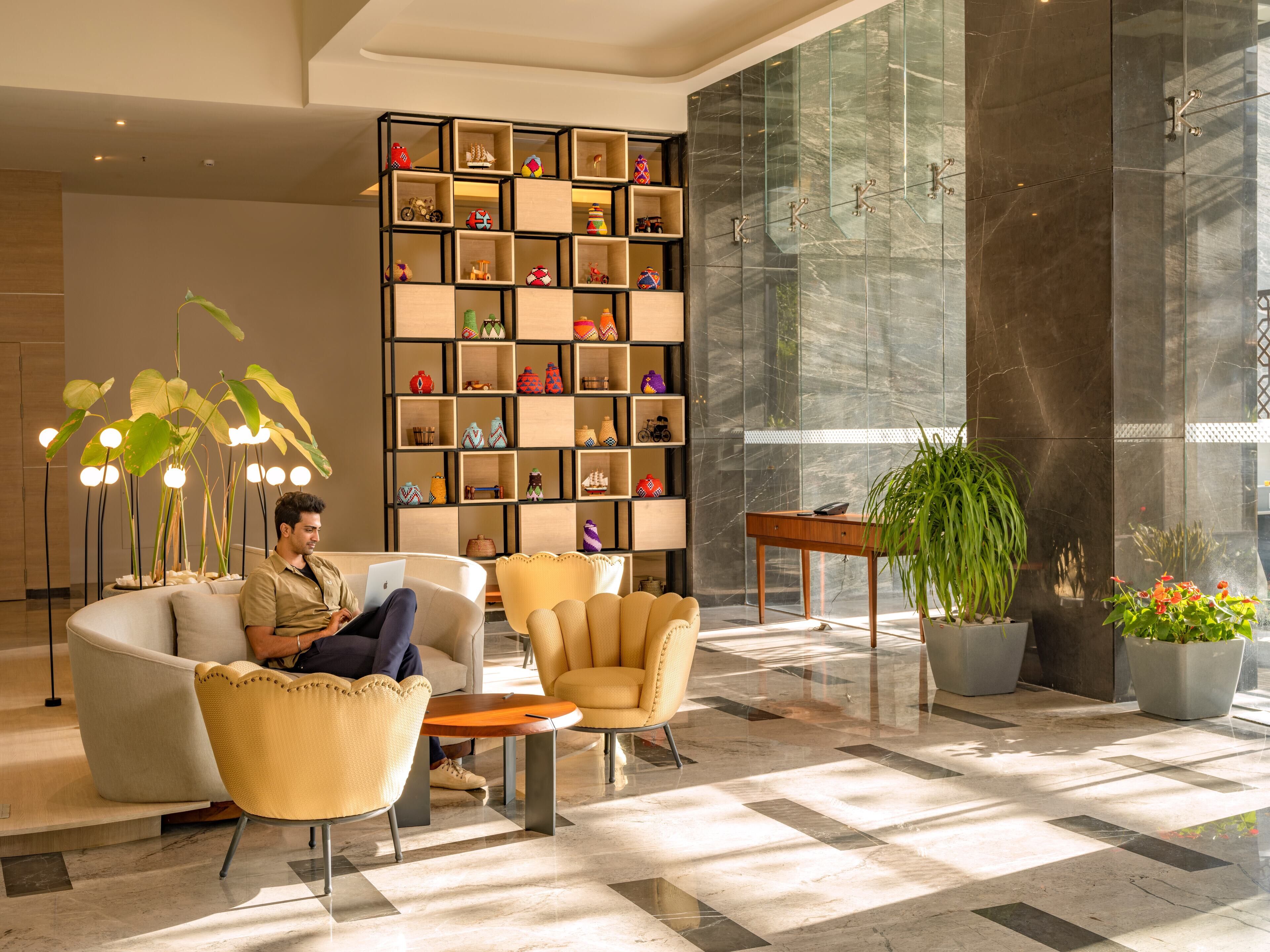 A modern lobby with a seating area, a decorative wall with shelves, and a large mirror.
